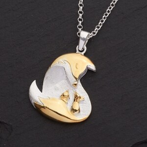 May include: A silver pendant necklace featuring a mother fox and two kits in a gold-tone finish. The pendant hangs from a delicate silver chain. The fox family is nestled together, creating a heartwarming scene.