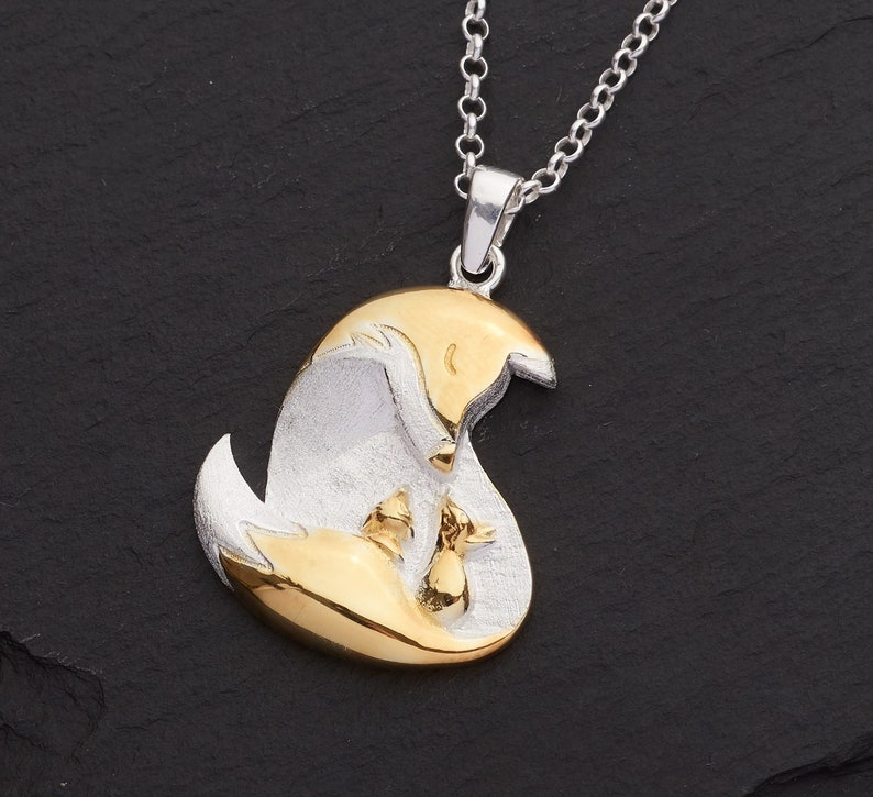 May include: A silver pendant necklace featuring a mother fox and two kits in a gold-tone finish. The pendant hangs from a delicate silver chain. The fox family is nestled together, creating a heartwarming scene.