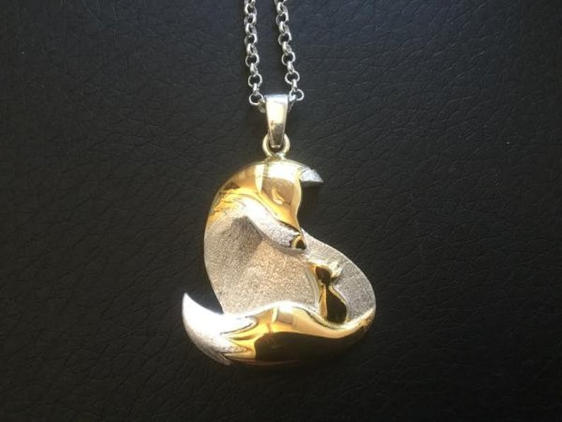 May include: Silver and gold-toned pendant necklace featuring a stylized fox design. The fox is depicted in a curled position, with intricate detailing. The pendant hangs from a delicate silver chain, creating an elegant accessory.
