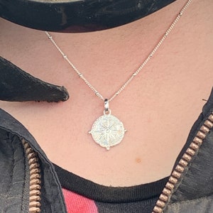 May include: A silver necklace with a compass pendant. The compass has a detailed design with a star in the centre.