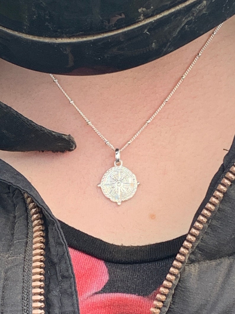 May include: A silver necklace with a compass pendant. The compass has a detailed design with a star in the centre.