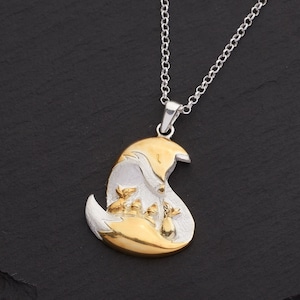 May include: A silver necklace with a pendant featuring a mother fox and three fox kits. The pendant has a gold-colored fox head and body, with silver accents. The chain is silver.