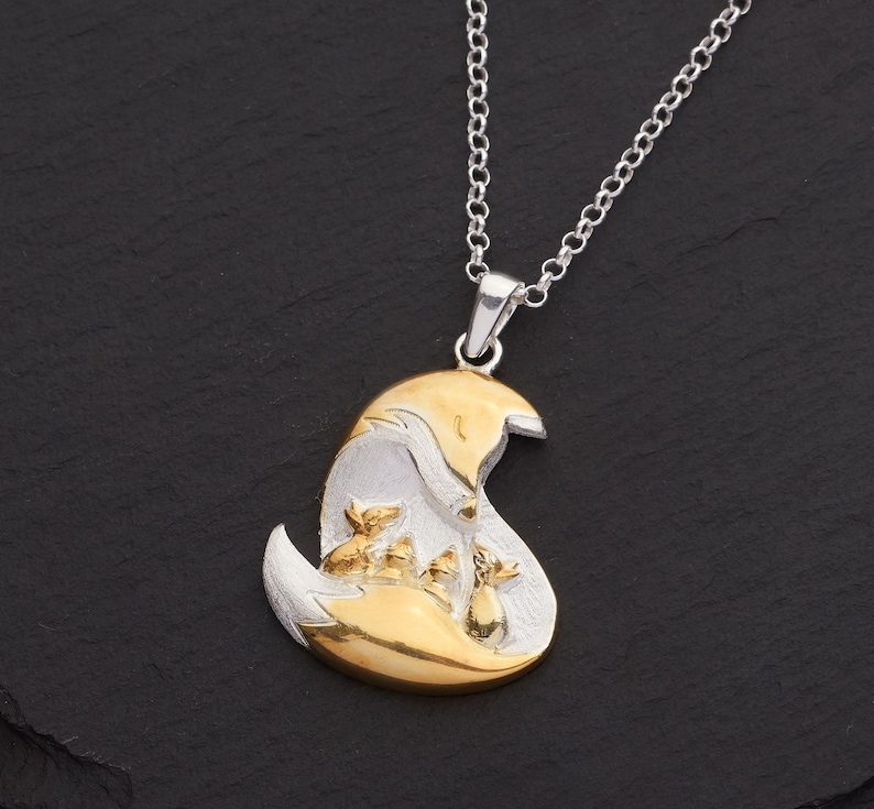May include: A silver necklace with a pendant featuring a mother fox and three fox kits. The pendant has a gold-colored fox head and body, with silver accents. The chain is silver.