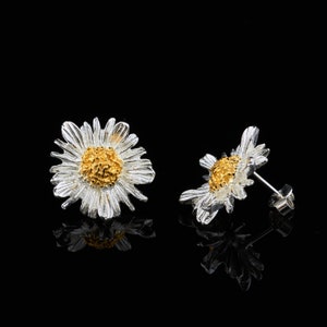 May include: A pair of silver daisy earrings with gold centres. The earrings are small and delicate, and they would make a lovely gift for a friend or loved one.