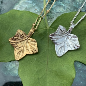 May include: Two necklaces featuring leaf-shaped pendants, one in a gold tone and one in a silver tone. Each pendant has a textured surface mimicking natural leaf veins and is attached to a delicate chain with small, evenly spaced metal beads.