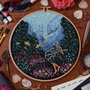 Lune sitting on a rock playing guitar underwater, surrounded by coral and glowing flowers. Fantasy cross stitch pattern inspired by a game scene