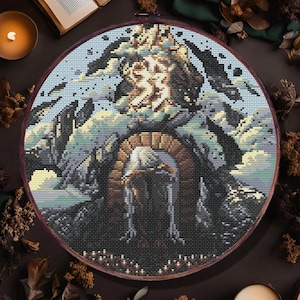 May include: A circular cross-stitch embroidery with a detailed landscape design, including an archway, set amongst candles and dried leaves. The text "pdf PATTERN" and "heiorun CRAFTS" are visible. The colour scheme features blues, browns, and creams.