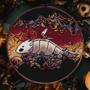 Puede incluir: Un patrón de punto de cruz en un bastidor de madera que presenta una criatura blanca con un cuerpo largo y una pequeña figura encima, sobre un fondo burdeos. El texto "pdf pattern" está en la parte superior y "heidora crafts" en la inferior.