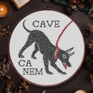 Könnte beinhalten: Ein schwarz-weißes Kreuzstichmuster eines schwarzen Hundes mit einer roten Leine, mit dem Text "Cave Canem" und "PDF Pattern" über dem Hund.