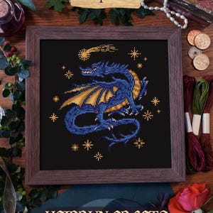 A PDF pattern for cross-stitching a blue dragon with gold wings against a dark blue background with gold stars. The pattern is titled "pdf pattern" and is by "heidrun crafts".