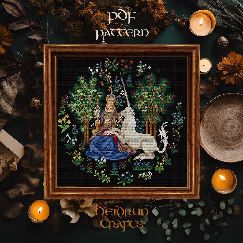 May include: A cross-stitch pattern featuring a woman in a blue gown sitting with a white unicorn in a forest setting. The pattern is framed in a brown wood frame and the text "PDF PATTERN" is above the frame. The text "HEIDRUN CRAFTS" is below the frame.