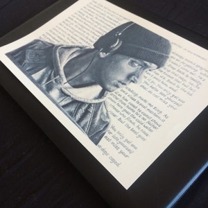 May include: A black and white illustration of a person wearing a black beanie and headphones. The image includes a quote: "retaking, make me king. As I'm close to post-mortem. It's either from home he's no father. On him coast to coast shows cause here goes the cold water. Schmoe who flows, he nose-riner. But the beat goes... You only get one, ter lose yourself, not miss your two dogs caged."