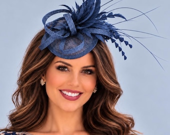 May include: A navy blue fascinator hat featuring structured loops and delicate feathers, paired with a cap-sleeve dress that has a sheer bodice overlay adorned with intricate navy blue and light blue floral embroidery on a beige base.