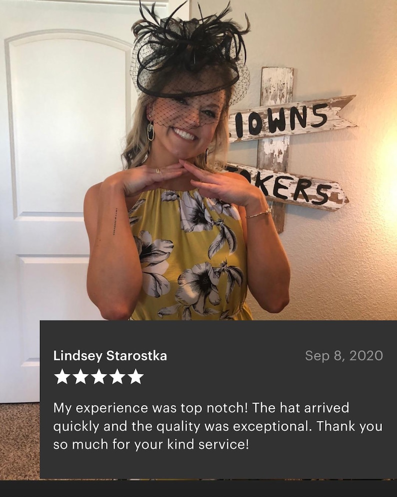 May include: A black fascinator hat featuring a decorative arrangement of feathers and a fine mesh veil that covers the upper face. The headpiece is paired with a sleeveless dress in a mustard yellow color, adorned with a large black and white floral print.