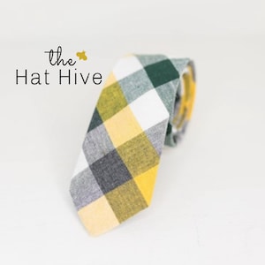 May include: A necktie with a yellow, green, white, and gray plaid pattern. The tie is rolled up and angled to the right. The text "the Hat Hive" is in the upper left corner.