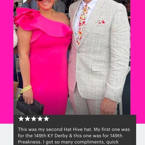 May include: A bright pink one-shoulder dress with a large ruffle detail paired with a matching pink and orange fascinator hat featuring netting. The ensemble is worn with black sunglasses and a black clutch, alongside a light grey plaid suit.