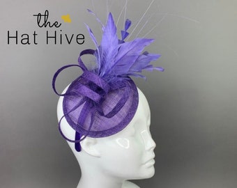 May include: A purple and lavender hat with a feather accent. The hat is on a white mannequin head. The text "the Hat Hive" is in the top left corner of the image.