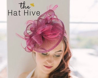 May include: A pink and purple fascinator with a large bow and feathers. The fascinator is made of a delicate mesh fabric.