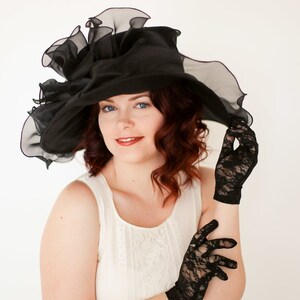 May include: A woman wearing a black lace hat with a large brim and black lace gloves. She is wearing a white lace dress.