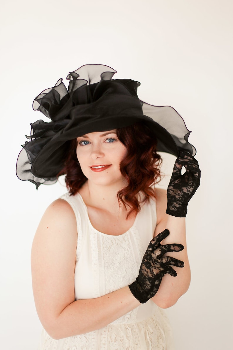 May include: A woman wearing a black lace hat with a large brim and black lace gloves. She is wearing a white lace dress.