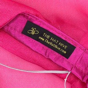 May include: A pink fabric hat with a black label that says "THE HAT HIVE" and "www.TheHatHive.com". A small bee icon is above the text.