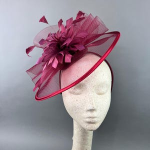 May include: A burgundy fascinator with a large feather and mesh detail. The fascinator is worn on a mannequin's head.