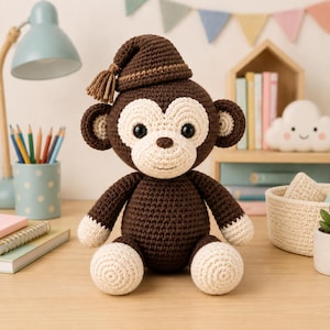 Puede incluir: Un peluche de mono tejido a ganchillo en color marrón oscuro con cara, manos y pies de color crema. El mono lleva un gorro de dormir a juego tejido a ganchillo en marrón oscuro con una pequeña borla en el lateral. Tiene ojos negros.