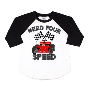 以下が含まれることがあります： 白と黒のベースボールスタイルのTシャツに、赤いレーシングカーと市松模様の旗が描かれています。シャツのテキストは「Need Four Speed」です。