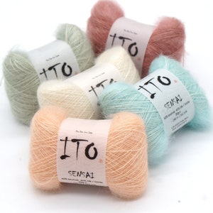 Peut inclure: Plusieurs pelotes de fil ITO Sensai aux couleurs pastel, pêche, rose, vert menthe et bleu. Chaque pelote porte une étiquette avec le nom de la marque et la composition. Le fil est doux et duveteux, idéal pour le tricot ou le crochet.