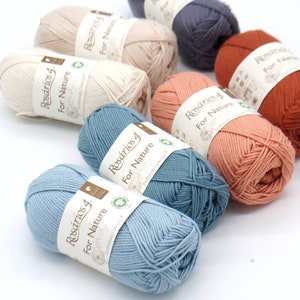 May include: A collection of yarn skeins in various colors, including light blue, beige, and rust. Each skein has a label that reads "Rosários 4 For Nature". The yarn is arranged on a white surface.