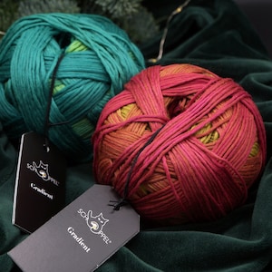 May include: Two balls of yarn, one teal green and one red with yellow and orange gradient, with black tags that say "Schappel" and "Gradient".
