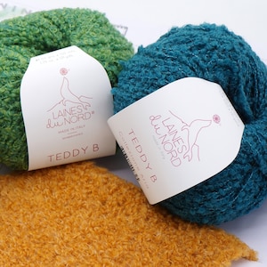 May include: Two balls of yarn in green and teal colours, with labels that read "Laines du Nord" and "Teddy B Collection Aria".