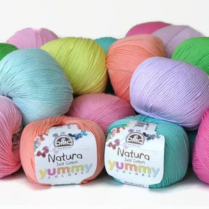 K&ouml;nnte beinhalten: Eine Sammlung bunter Wollkn&auml;uel in den Farben Rosa, Gr&uuml;n, Blau und Orange. Das Garn ist mit "Natura Just Cotton Yummy Colors" gekennzeichnet und wird von DMC hergestellt.