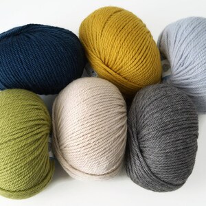 May include: Six balls of yarn in different colors: green, yellow, blue, gray, beige, and light blue. The yarn is arranged in a circle.