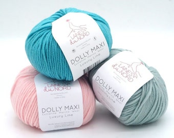 May include: Three balls of yarn in different colors: turquoise, pink, and light green. Each ball has a label that reads "Dolly Maxi Extrafine Merino Wool Luxury Line" and the brand name "Laines du Nord".