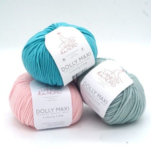 May include: Three balls of yarn in different colours: turquoise, pink, and light green. Each ball has a label that reads "Dolly Maxi Extrafine Merino Wool Luxury Line" and the brand name "Laines du Nord".