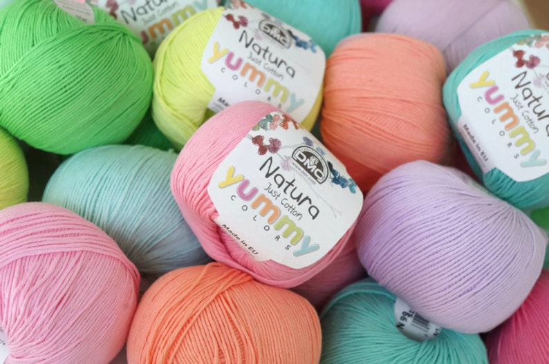 K&ouml;nnte beinhalten: Eine Sammlung bunter Wollkn&auml;uel in den Farben Gr&uuml;n, Gelb, Rosa, Orange und Lila. Jede Kn&auml;uel hat ein Etikett mit der Aufschrift "Natura Just Cotton Yummy Colors" und "Made in EU".