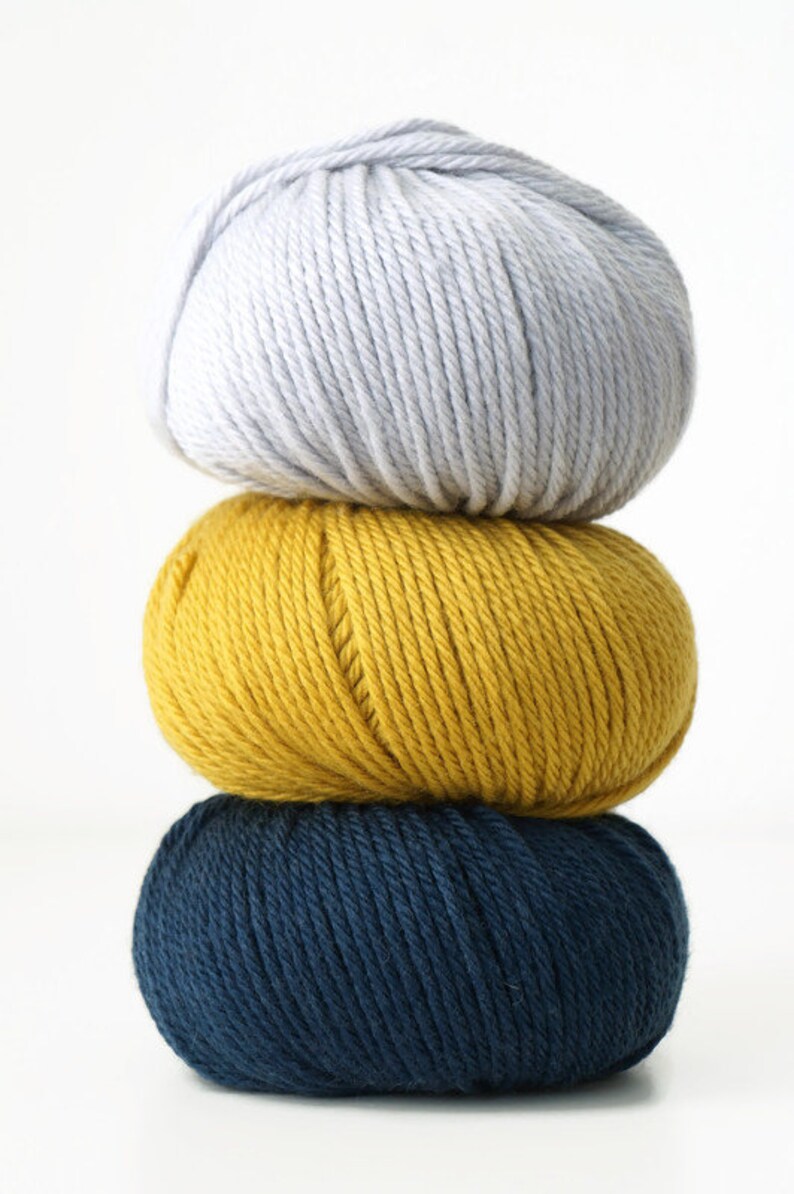 May include: Three balls of yarn stacked on top of each other. The top ball is light gray, the middle ball is yellow, and the bottom ball is dark blue.