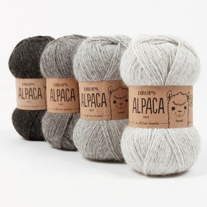 May include: Four skeins of yarn in different shades of gray, brown, and white. Each skein has a brown label with the text "DROPS ALPACA MIX" and a cartoon alpaca.