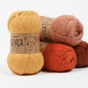 May include: Four skeins of Drops Alpaca yarn in different shades of orange, yellow, and brown. The yarn is labeled "Drops Alpaca Uni Colour" and features a cartoon alpaca on the label.
