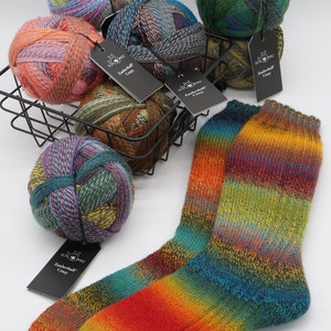 May include: Five balls of colorful yarn in a wire basket with a pair of rainbow striped socks. The yarn is labeled "Zauberball Crazy".