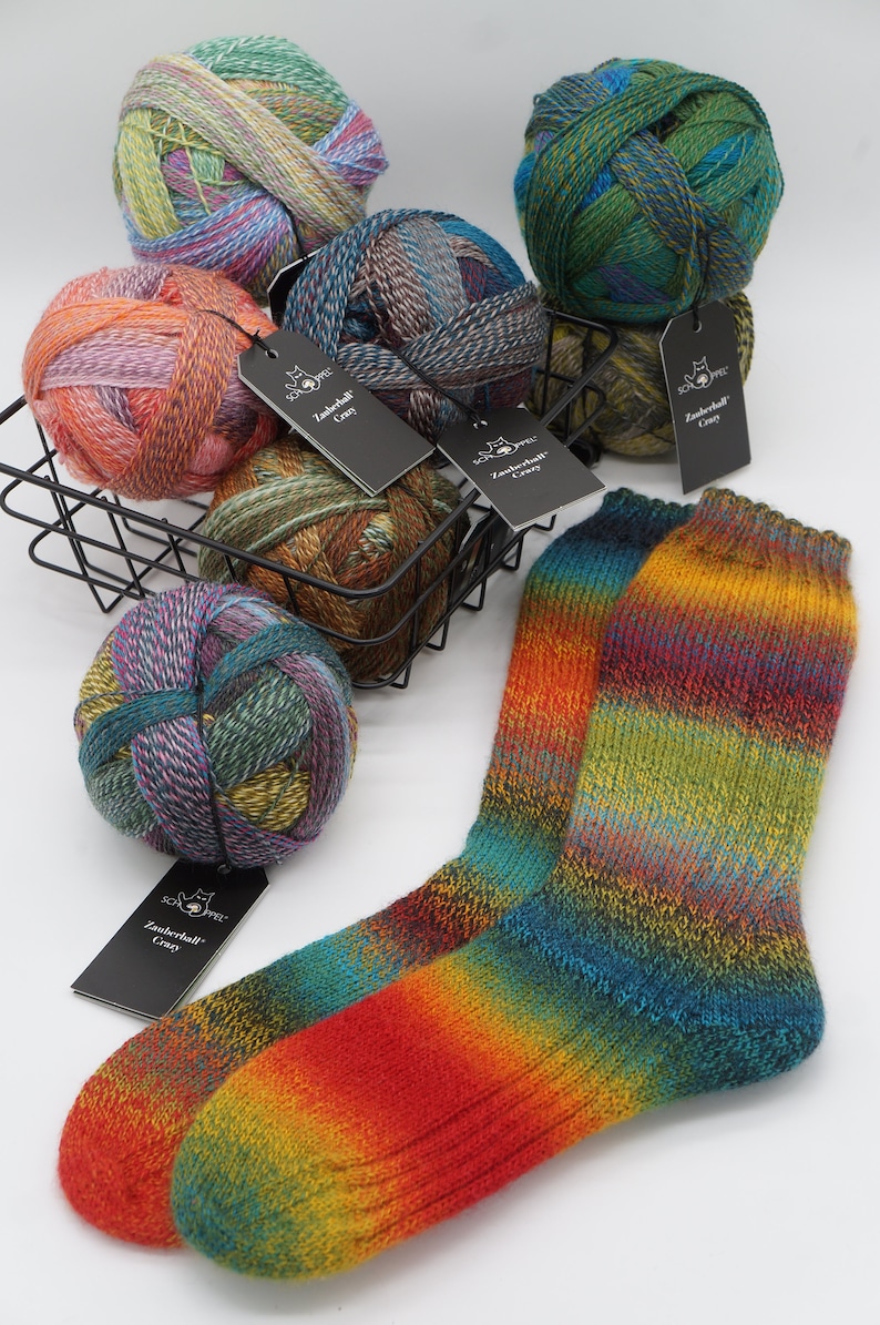 May include: Five balls of colorful yarn in a wire basket with a pair of rainbow striped socks. The yarn is labeled "Zauberball Crazy".