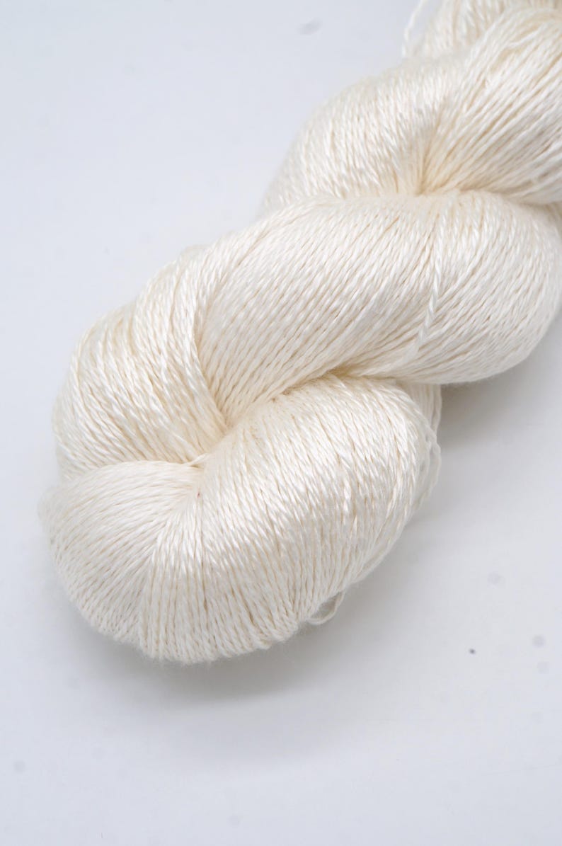 May include: A skein of off-white yarn, tightly wound and textured. The yarn appears soft and has a slight sheen, suggesting a natural fiber. Ideal for knitting or crochet projects.