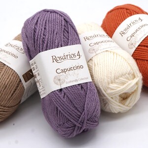 May include: Four skeins of yarn in different colours: brown, purple, white, and orange. Each skein has a label that reads "Ros&aacute;rios 4 Cappuccino Ecofriendly Collection".