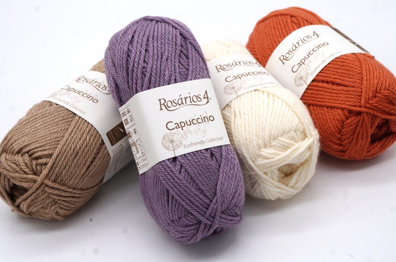 May include: Four skeins of yarn in different colours: brown, purple, white, and orange. Each skein has a label that reads "Ros&aacute;rios 4 Cappuccino Ecofriendly Collection".