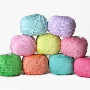 K&ouml;nnte beinhalten: Eine Sammlung von acht Garnkn&auml;uel in verschiedenen Pastellfarben, darunter Rosa, Gr&uuml;n, Blau und Gelb. Die Kn&auml;uel sind in Pyramidenform angeordnet.