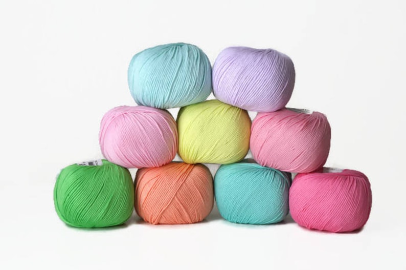 K&ouml;nnte beinhalten: Eine Sammlung von acht Garnkn&auml;uel in verschiedenen Pastellfarben, darunter Rosa, Gr&uuml;n, Blau und Gelb. Die Kn&auml;uel sind in Pyramidenform angeordnet.