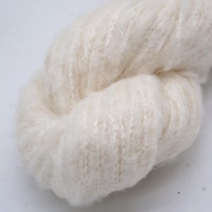 May include: Close-up of a skein of cream-coloured yarn. The yarn has a soft, fluffy texture with a slightly textured surface. The fibres are tightly spun, creating a dense, yet airy appearance. Suitable for knitting or crochet projects.