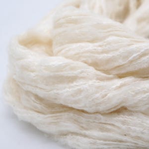 May include: Close-up of a bundle of cream-coloured yarn. The yarn has a soft, fluffy texture and a slightly textured surface. The fibres are loosely spun, giving it a light and airy appearance. Suitable for knitting or crochet projects.