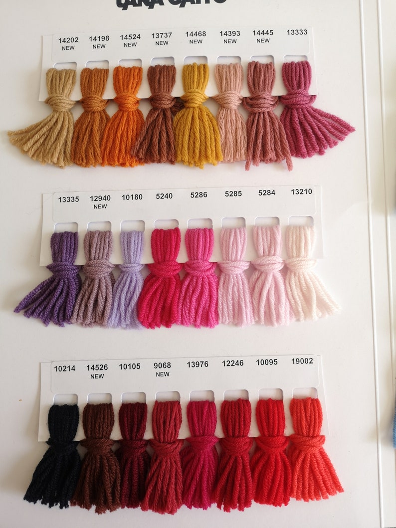 Puede incluir: Una carta de colores con muestras de hilo en varios tonos de marr&oacute;n, naranja, rojo, rosa, morado y negro. Las muestras de hilo est&aacute;n dispuestas en filas y columnas, con cada muestra etiquetada con un n&uacute;mero.